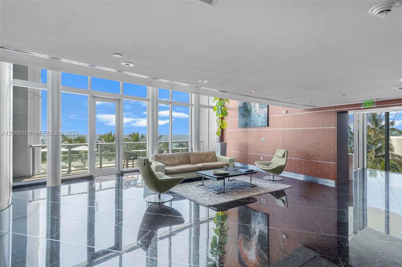 Condominium lounge with floor-to-ceiling windows overlooking palm trees and the ocean.