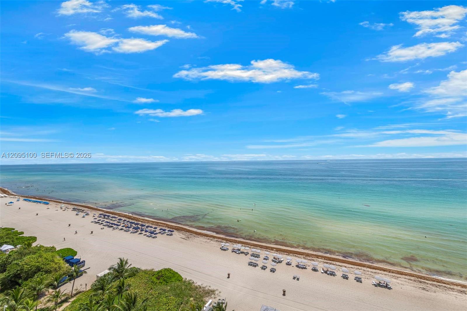Sandy beach and turquoise ocean with rows of umbrellas along the shoreline.