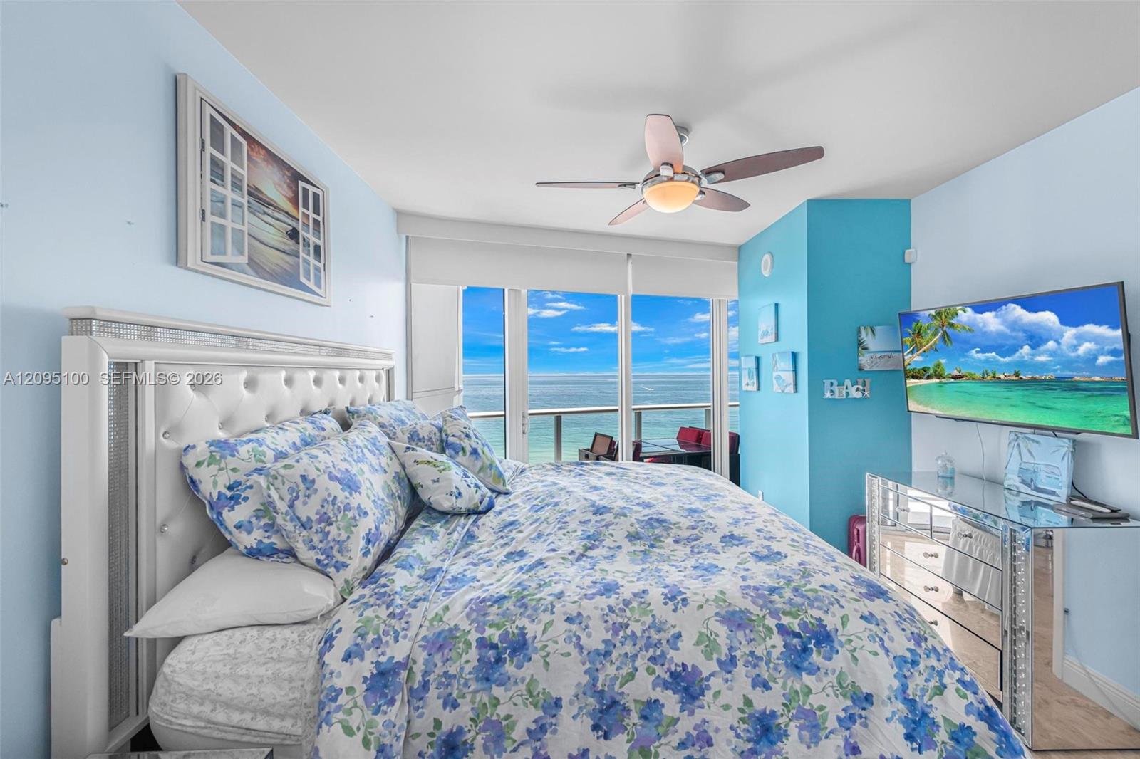 Furnished bedroom with blue floral bedding and sliding doors overlooking the ocean.