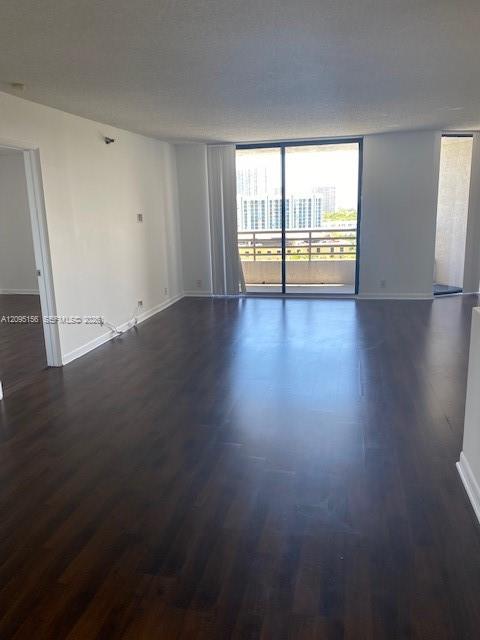 Empty living room with dark wood floors and sliding doors to a balcony.