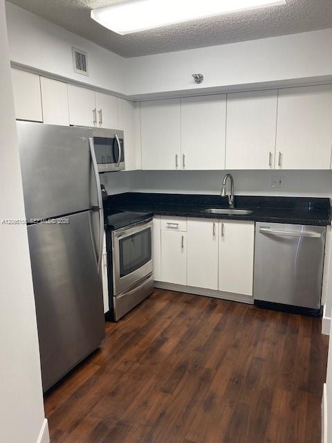 Kitchen with white cabinets, dark counters, stainless steel appliances, and wood-look flooring.