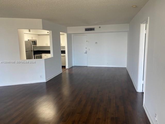 Vacant apartment living area with dark wood floors and a kitchen pass-through.