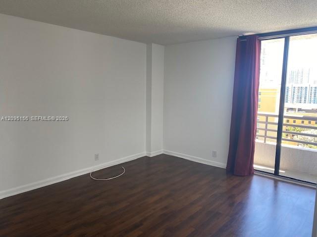 Vacant room with dark wood floors and sliding glass doors opening onto a balcony overlooking high-rise buildings.