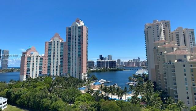 Waterfront high-rise condominiums overlooking a bay, with boats, palm trees, and distant buildings.