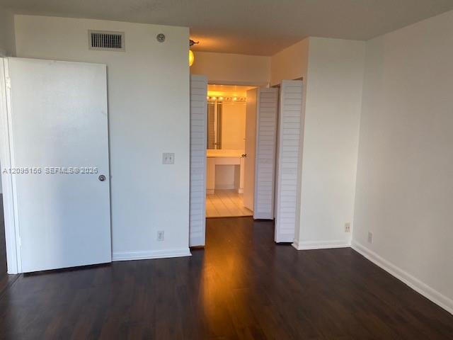 Vacant bedroom with dark hardwood floors and an open doorway to a lit vanity area.