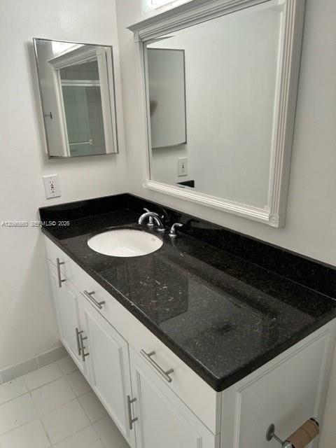 Bathroom vanity with a black stone countertop, oval sink, white cabinets, and large mirrors.