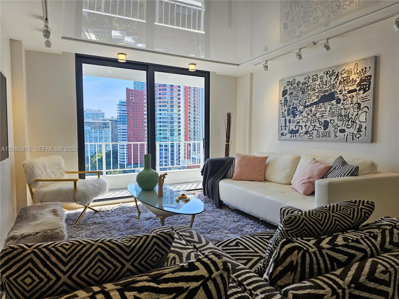 Furnished living room with patterned chairs and large windows overlooking downtown high-rises.