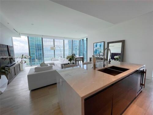 Modern kitchen island overlooking a furnished living area and floor-to-ceiling city windows.