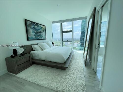 Bedroom with a low platform bed and floor-to-ceiling windows overlooking Miami buildings.