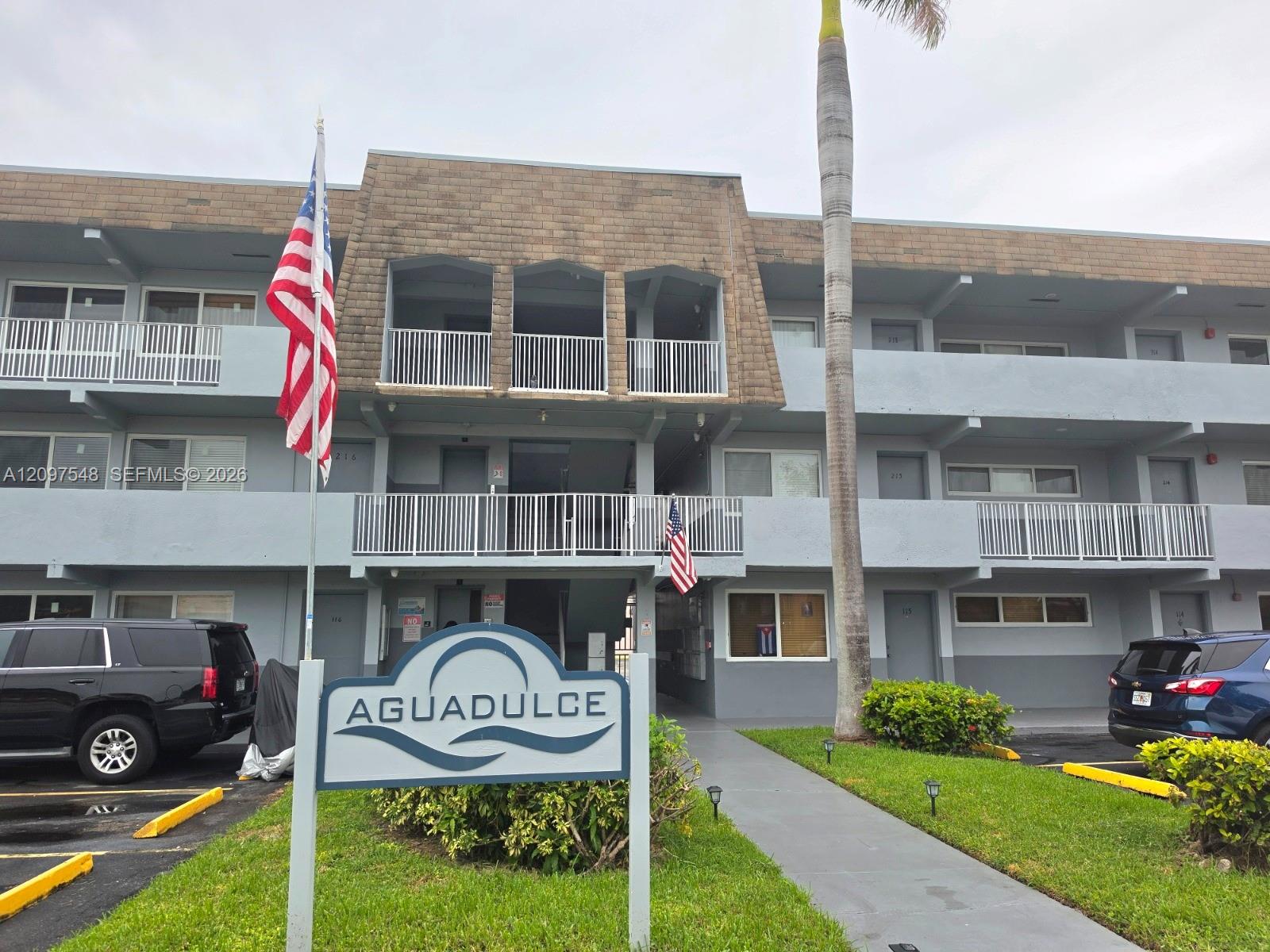 Aguadulce condominium exterior with white balconies, an American flag, and a sign by the entrance.