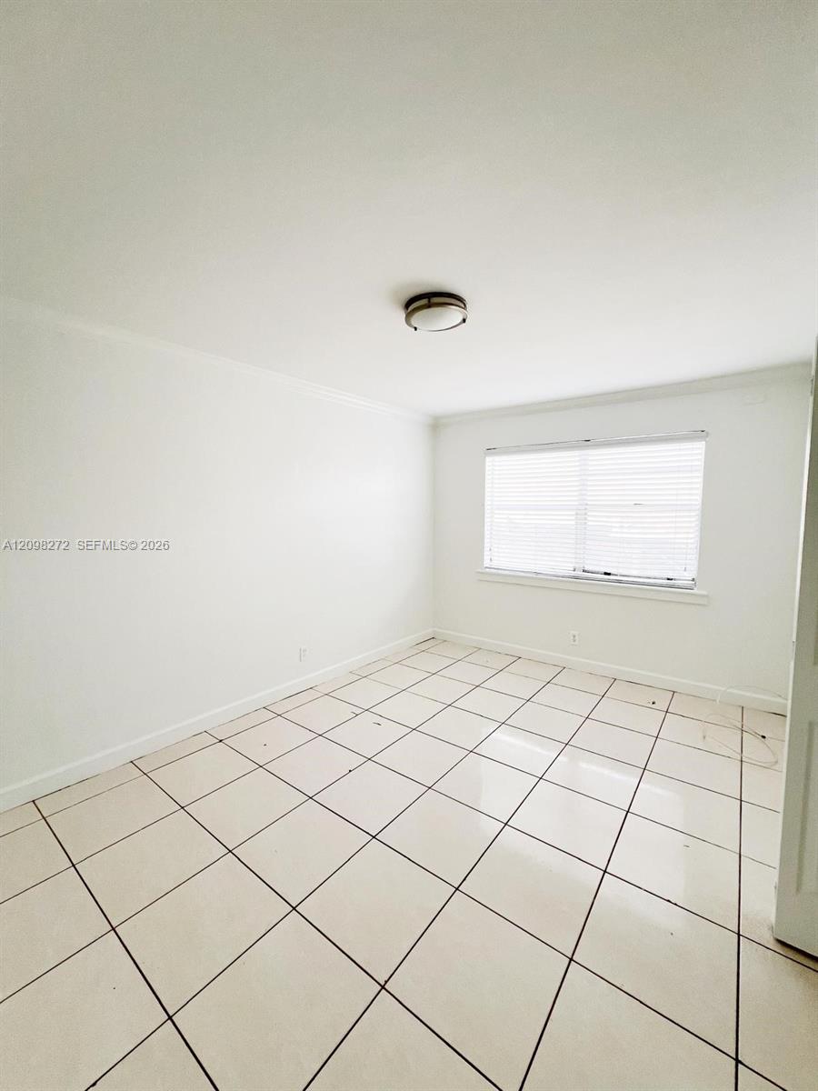 Empty room with large white tile floors and a window with closed blinds.