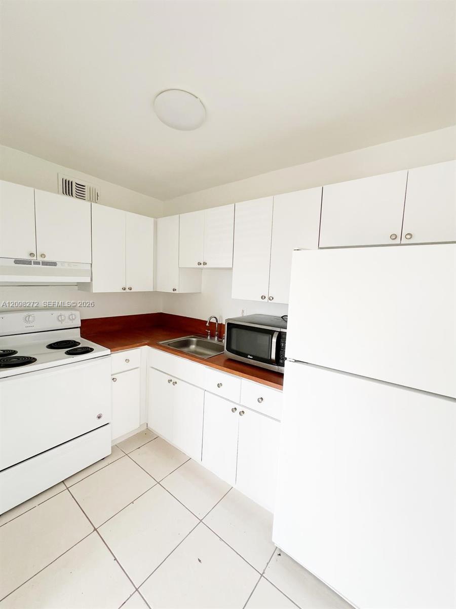Kitchen with white cabinets, reddish-brown countertops, and white appliances.