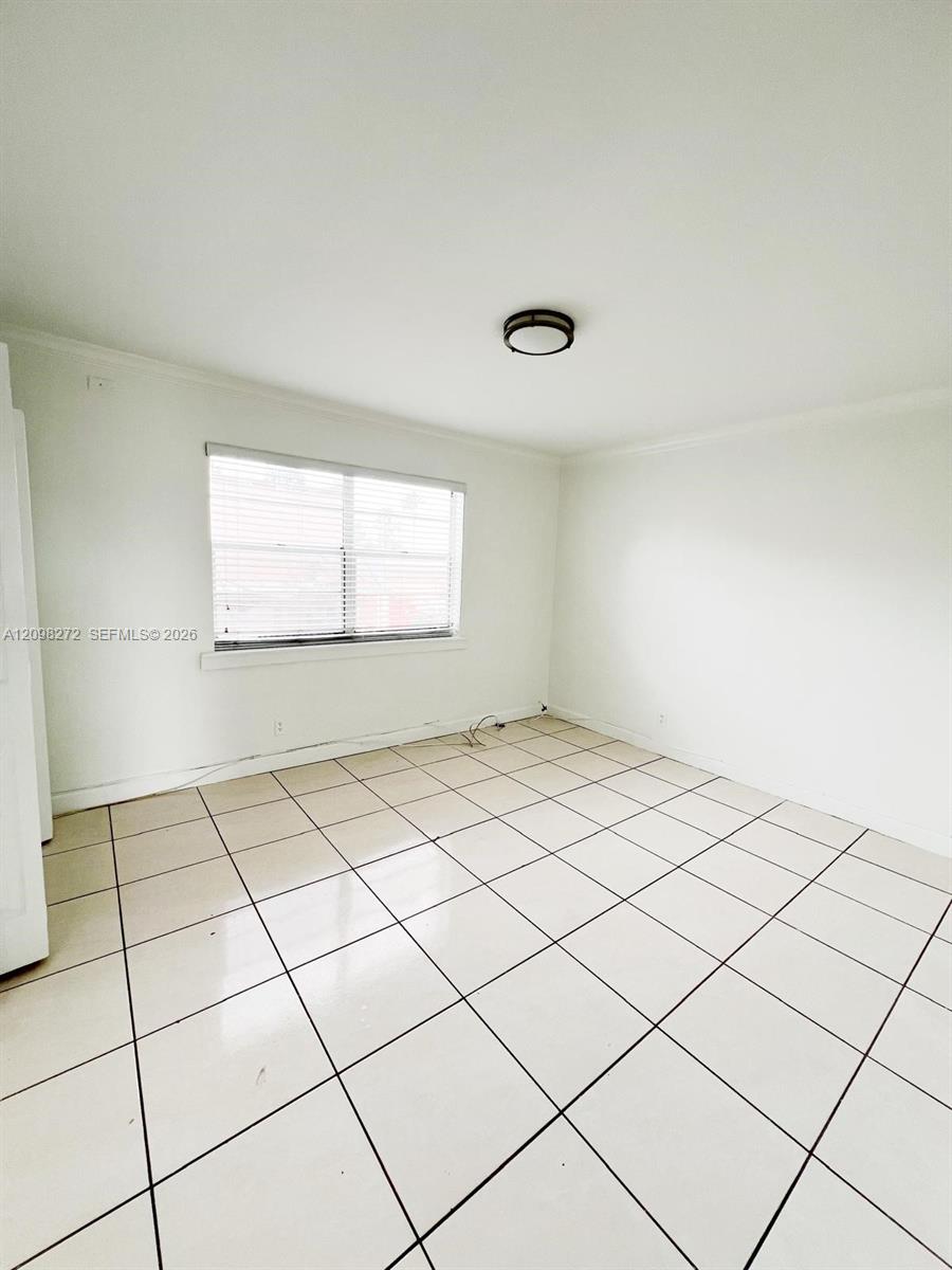 Vacant tiled room with a wide window, white blinds, and a ceiling light.