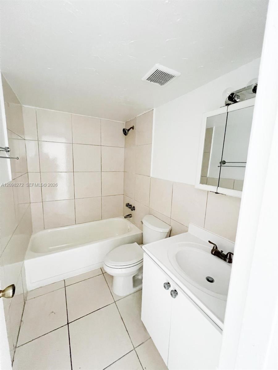 Bathroom with a tiled bathtub, toilet, and white vanity with mirrored cabinet.