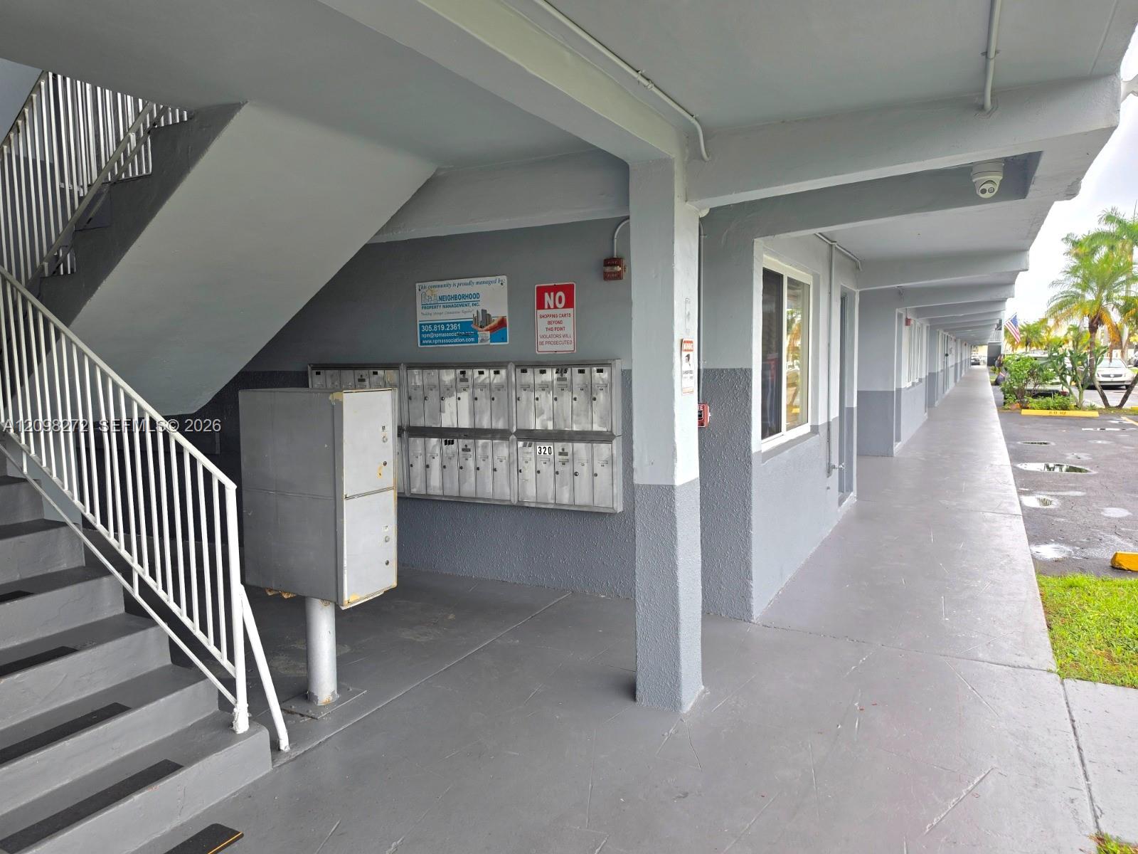 Apartment building exterior walkway with stairs, mailboxes, and a parking area.