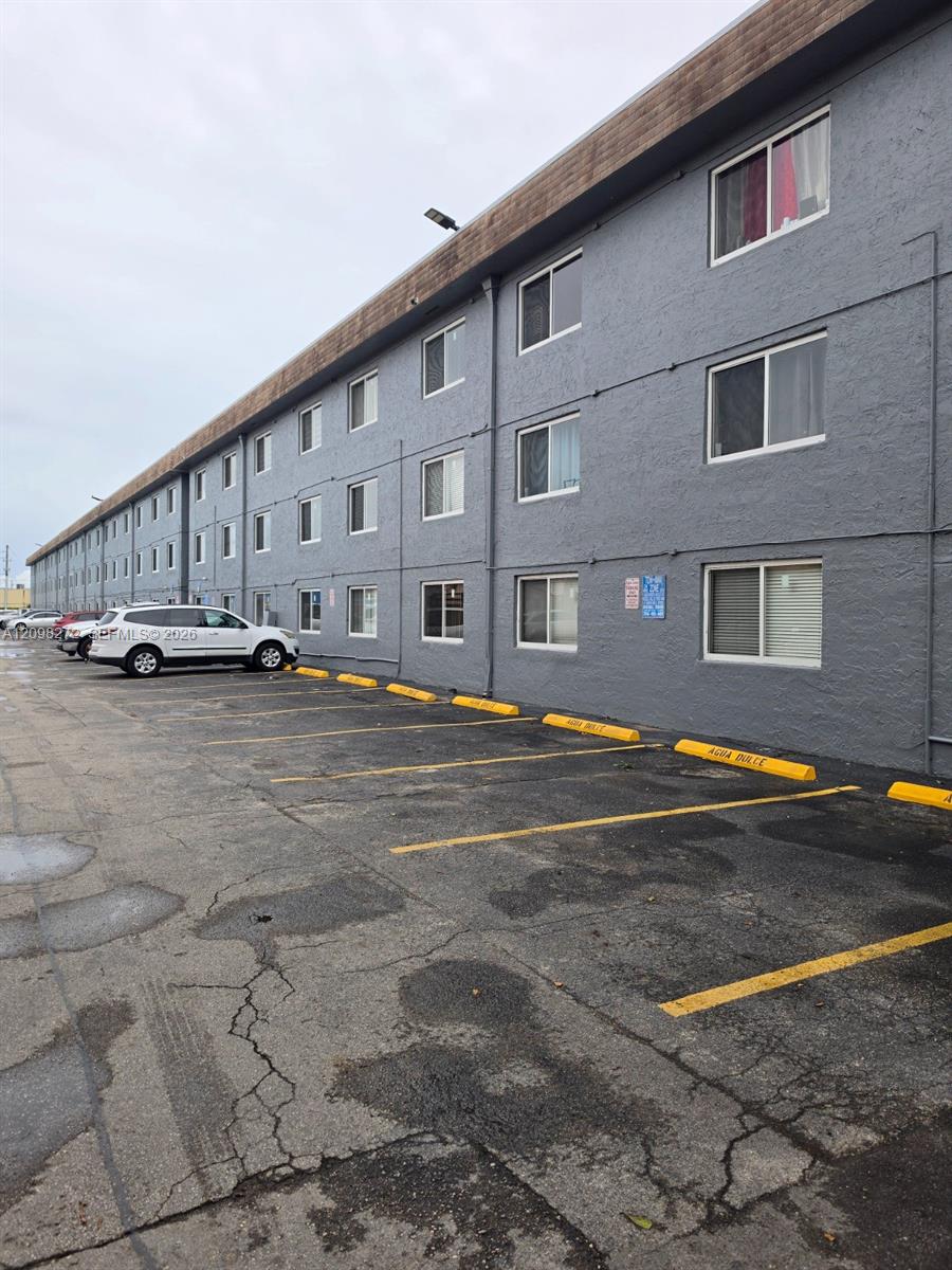Three-story gray apartment building beside a cracked parking lot with yellow lines and a white SUV.