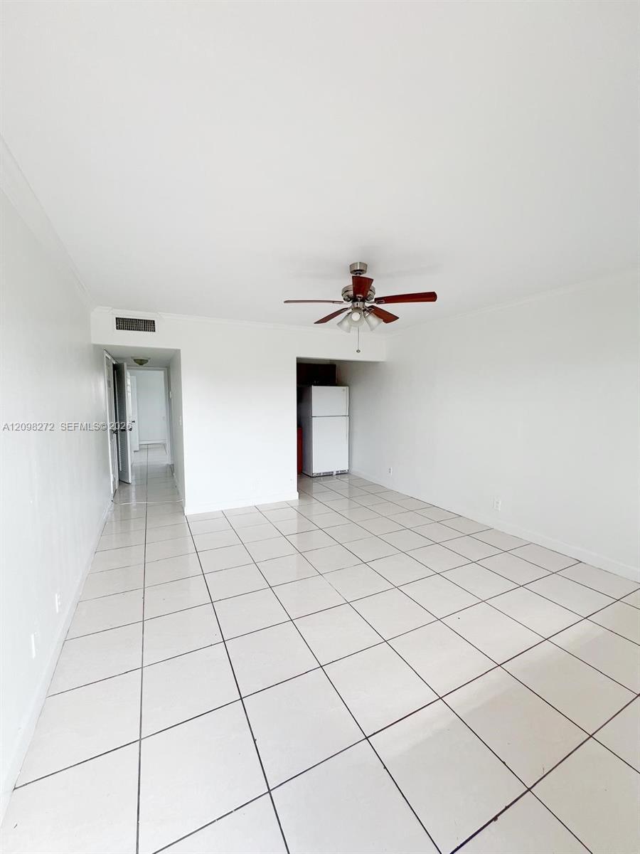 Vacant living room with large white tile floors, a ceiling fan, and a refrigerator nook.