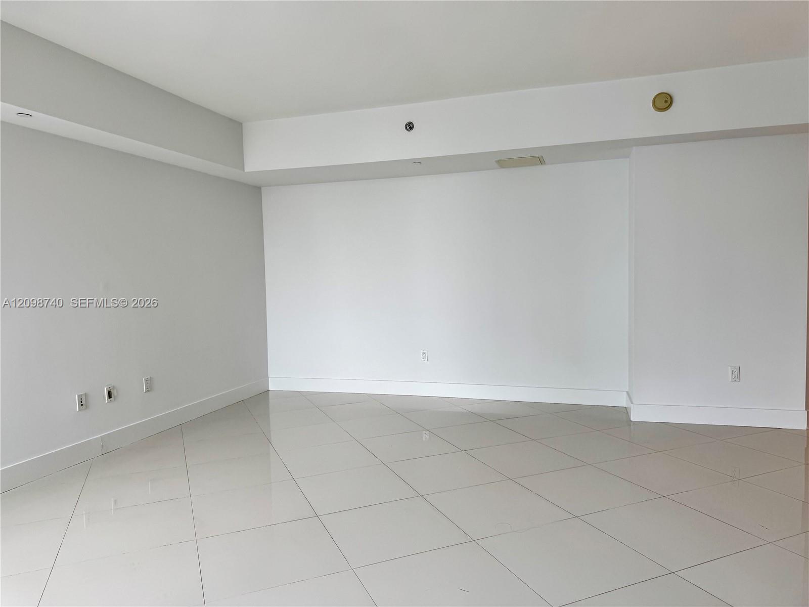Vacant condo room with large light tile flooring and a recessed ceiling.