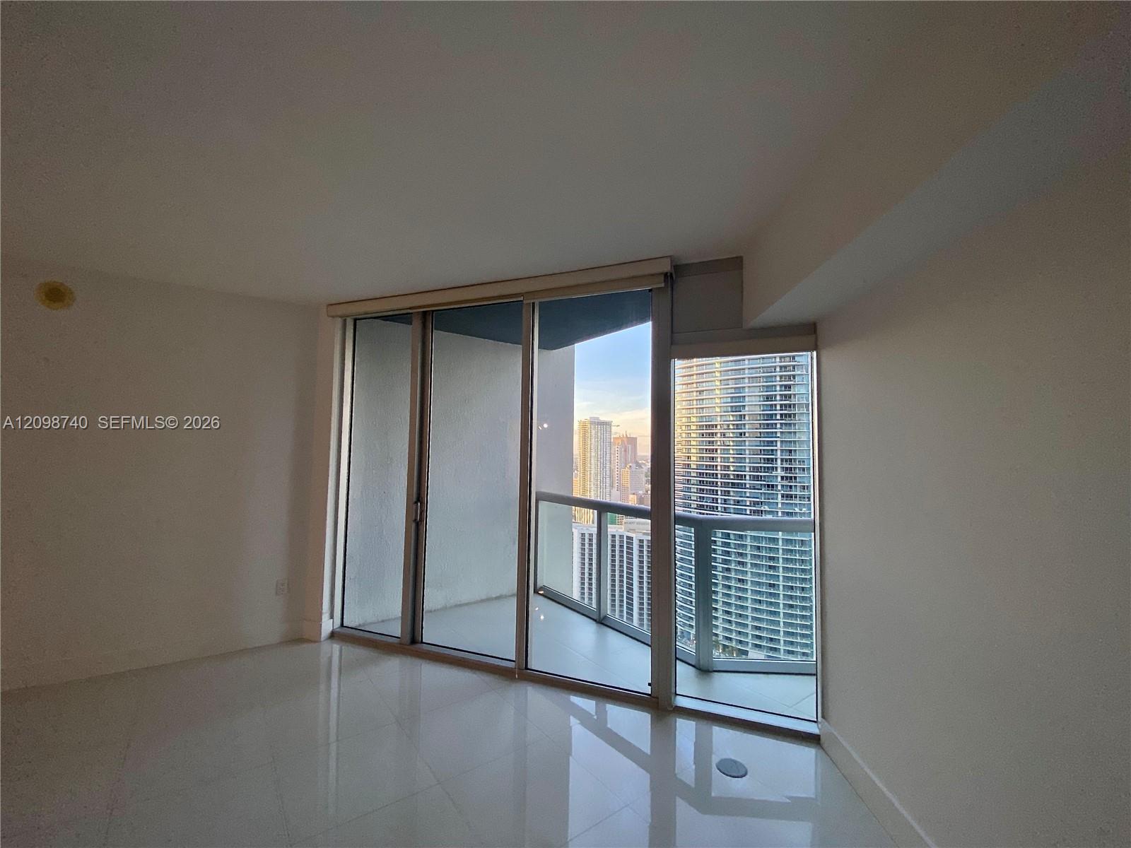 Vacant condo interior with glossy tile floors, a glass balcony, and views of neighboring towers.