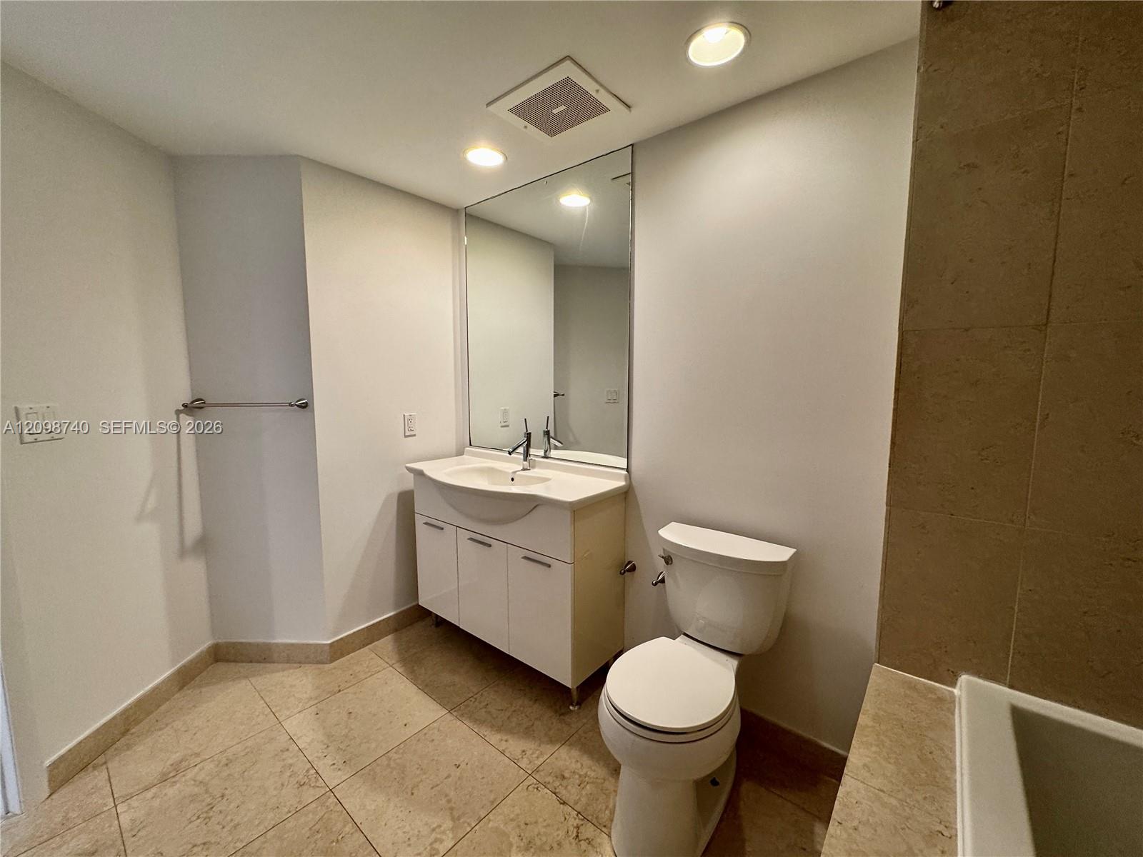 Bathroom with a white vanity and mirrored cabinet, toilet, and beige stone tile.