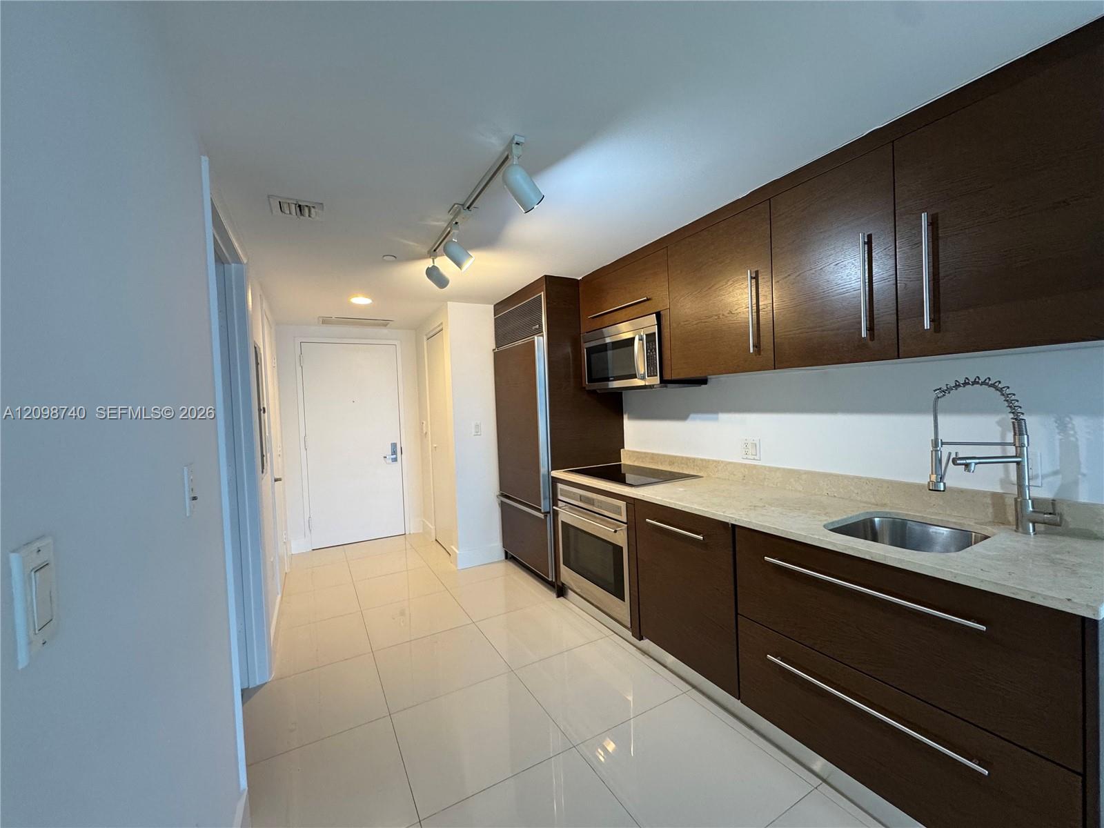 Modern condo kitchen with dark wood cabinets, stainless steel appliances, and a light stone countertop.