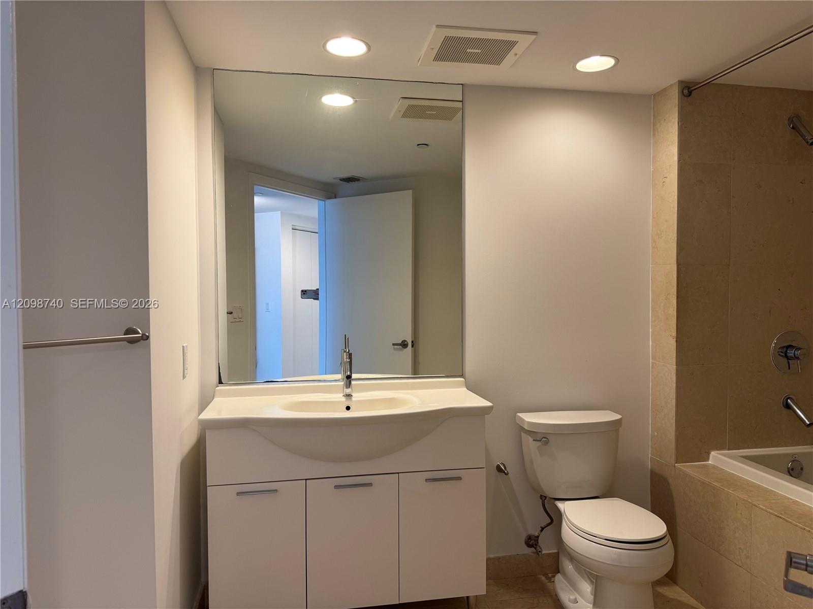 Bathroom with a white vanity, large mirror, toilet, and tan tiled tub and shower.