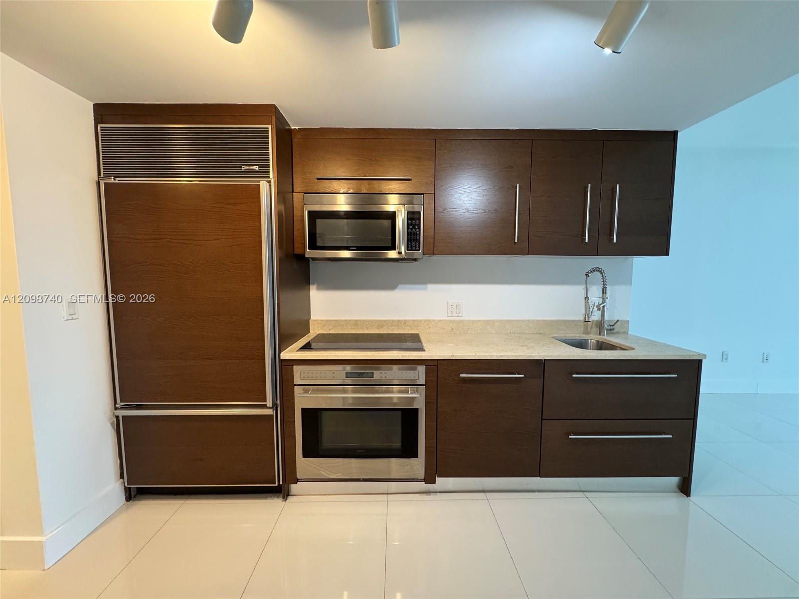 Condo kitchen with dark wood cabinetry, stainless steel appliances, and a pale stone countertop.