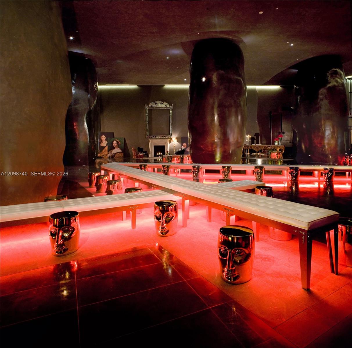 Dramatic lounge with white benches, reflective stools, red lighting, and oversized dark columns.