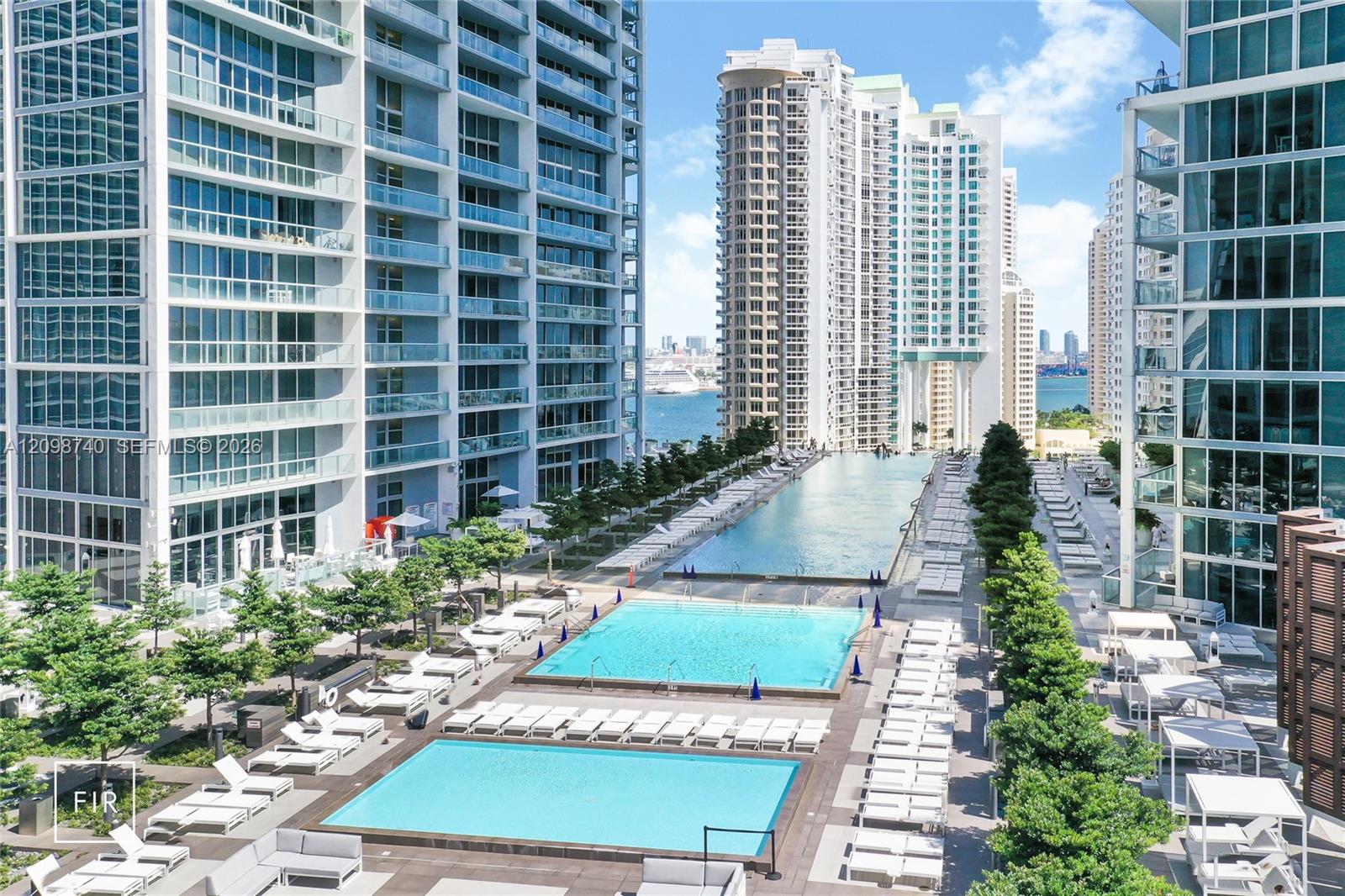 Two rooftop pools between modern towers, with lounge chairs and a view of the bay.