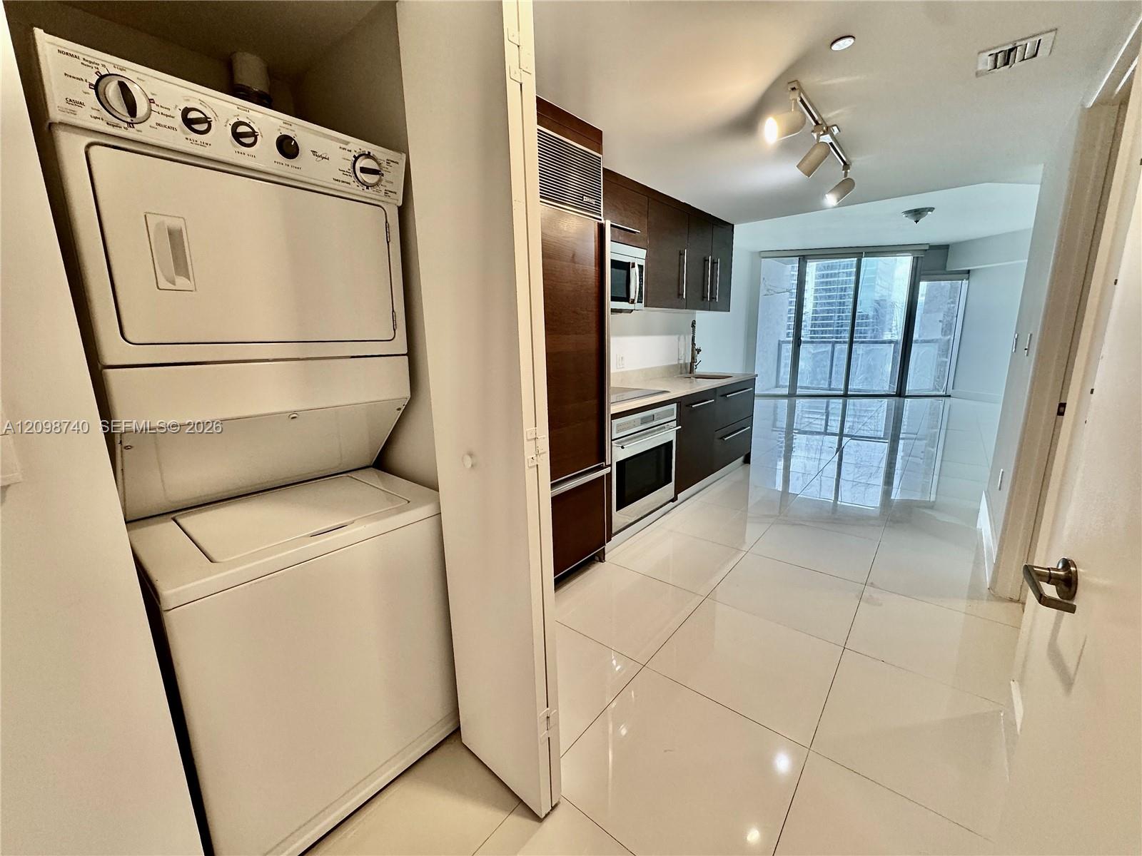 Kitchen and laundry area with stacked washer-dryer, dark cabinetry, and sliding glass doors.