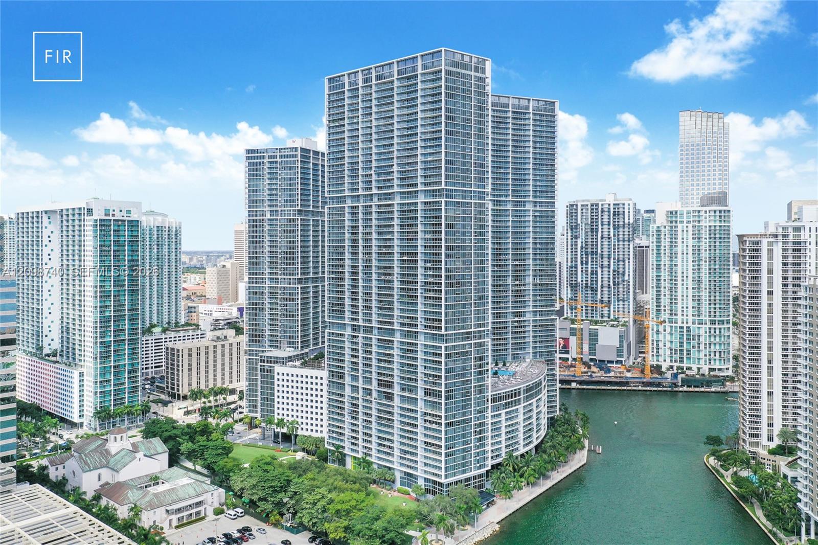 Glass high-rise condominium towers along a Miami waterway, with downtown buildings and greenery.