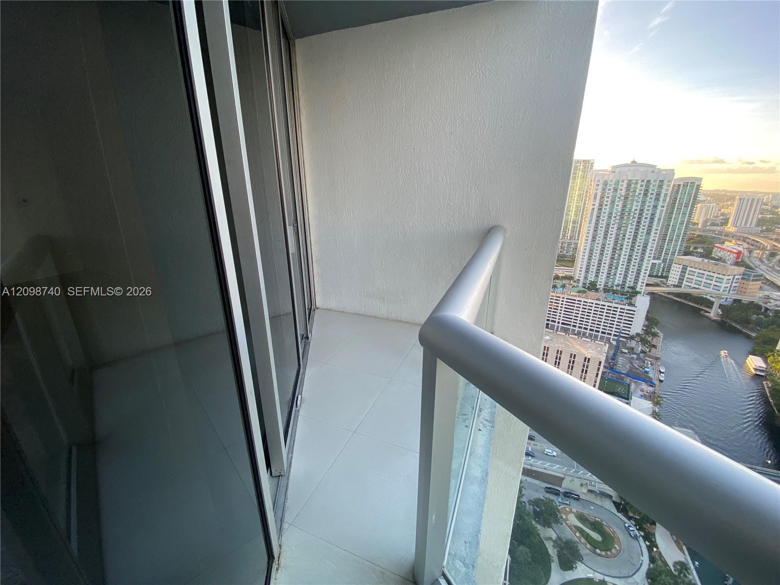High-rise balcony overlooking Miami buildings and a waterway, with tiled flooring and a glass railing.