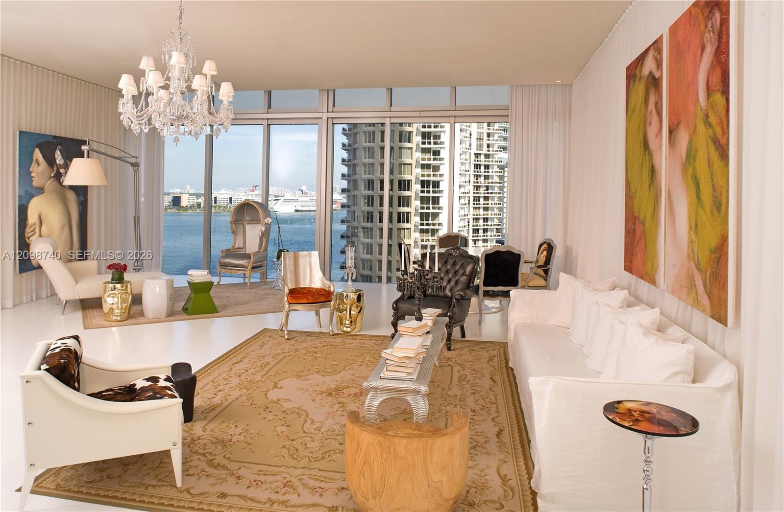 Furnished condo living room with a chandelier and floor-to-ceiling windows overlooking the water.