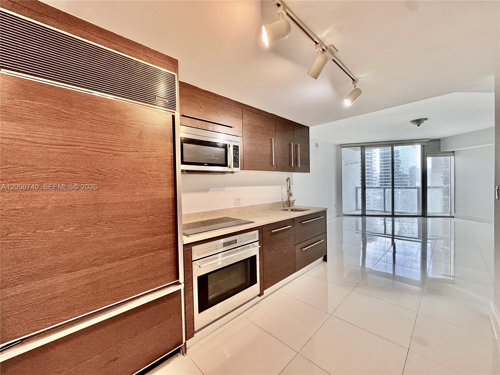 Modern condo kitchen with wood cabinetry and stainless-steel appliances, opening onto a balcony with city views.