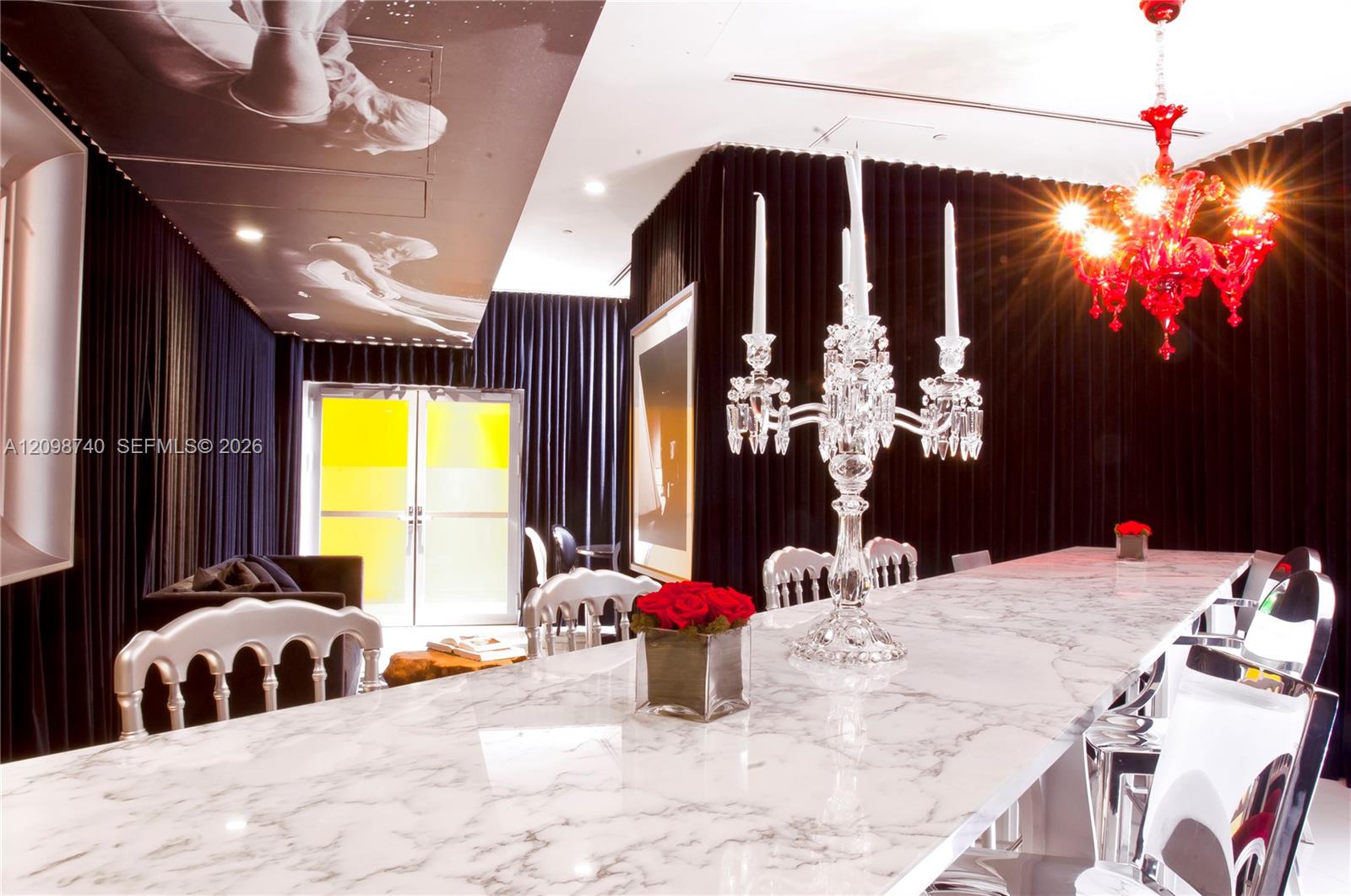 Dining room with a long marble table, crystal candleholders, and a striking red chandelier.