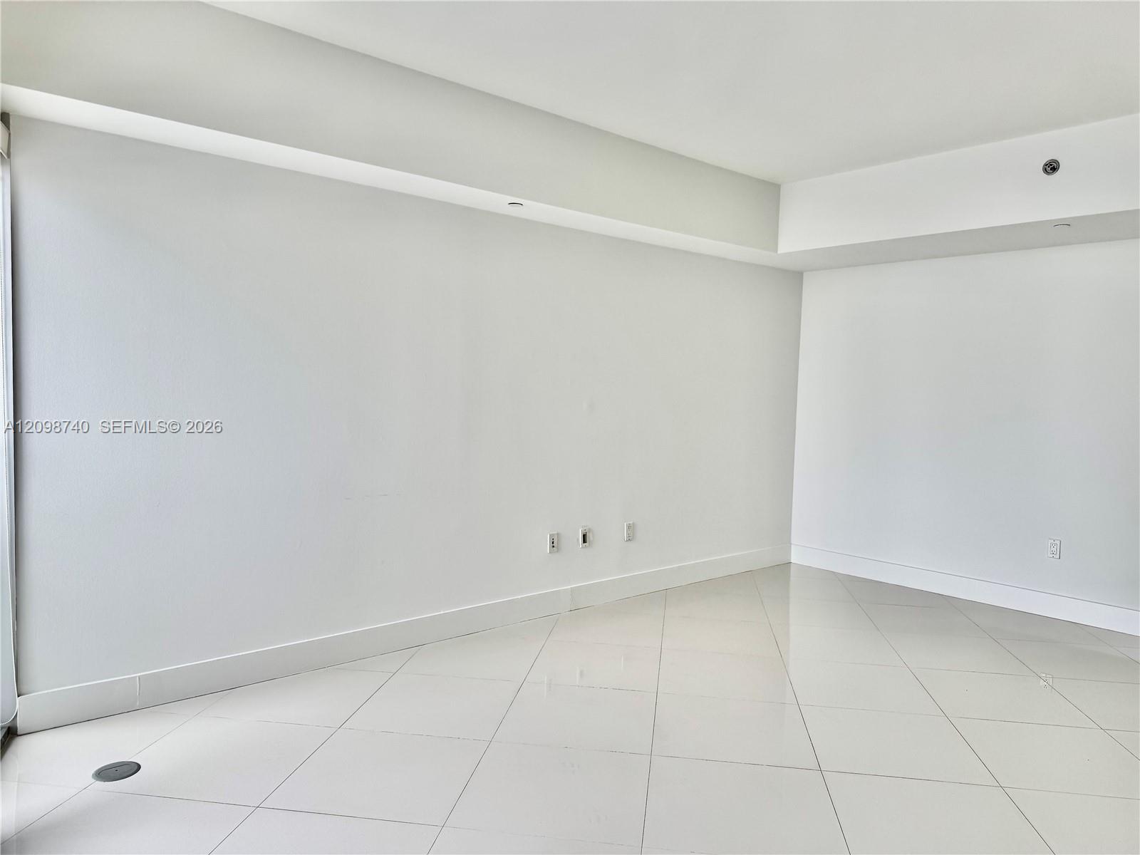 Empty condominium room with pale tile floors and a stepped ceiling.