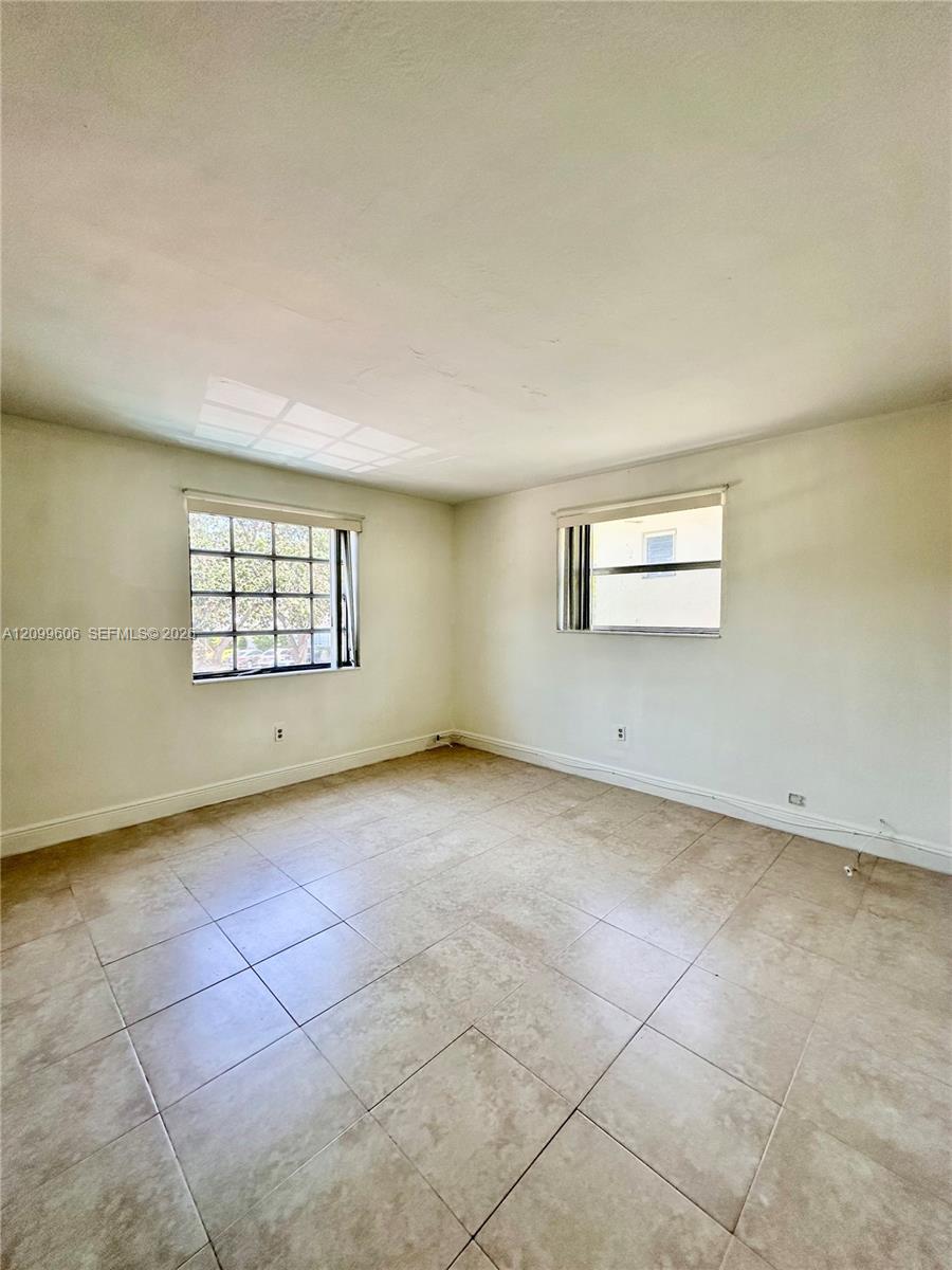 Empty room with beige tile flooring, two windows, and marks on the ceiling.