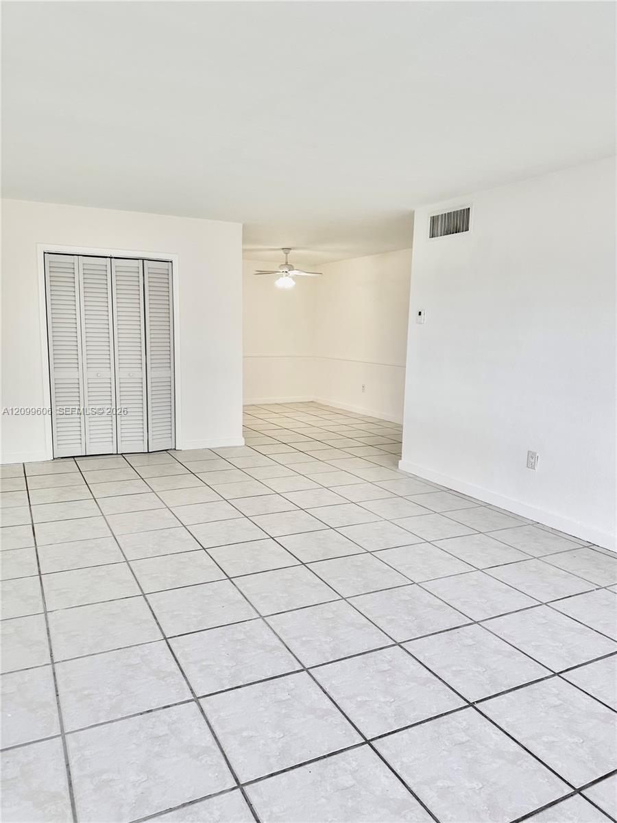 Empty living and dining area with large light tile floors, louvered closet doors, and a ceiling fan.