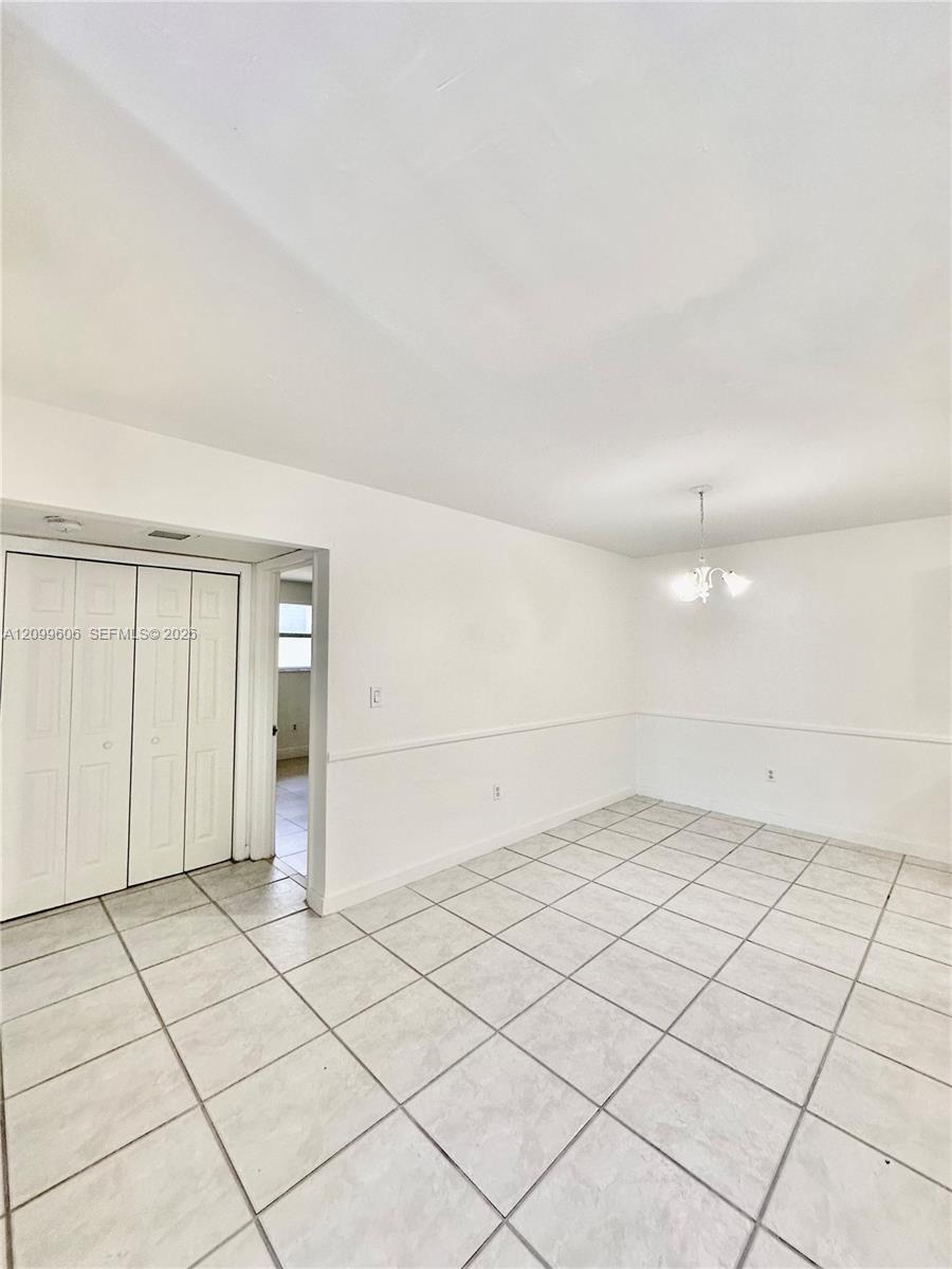 Empty tiled room with white walls, closet doors, and a small chandelier.