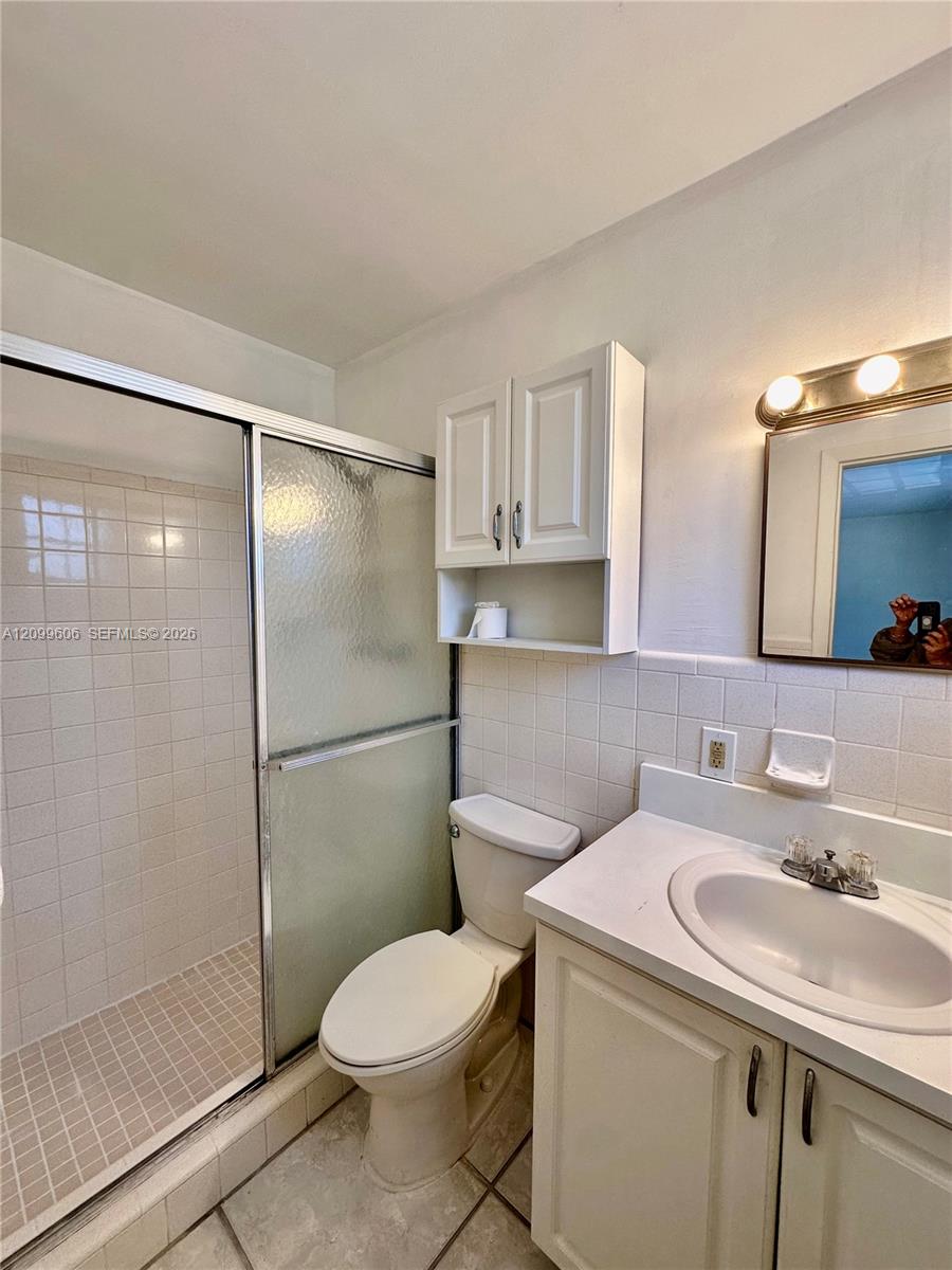 Bathroom with a frosted-glass shower, toilet, and white vanity with oval sink.