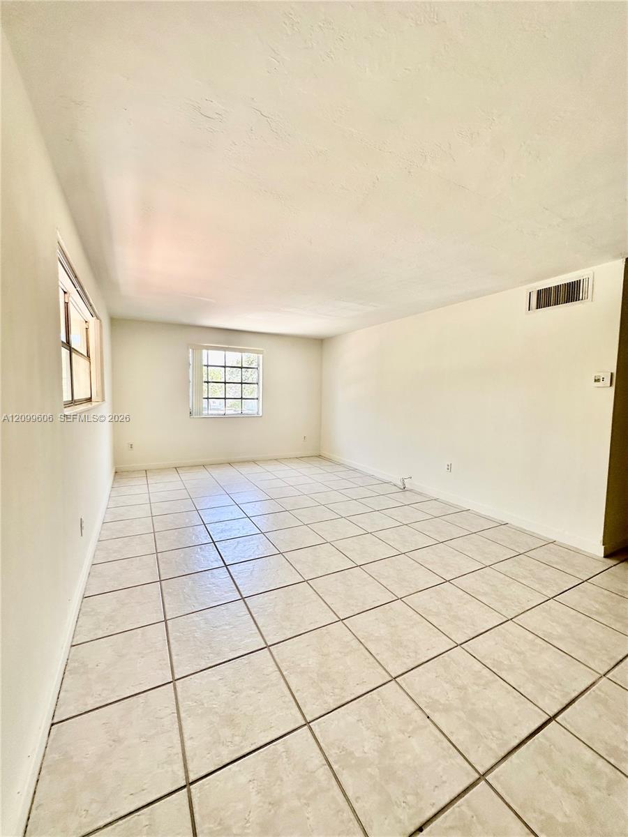 Empty living room with beige tile flooring and windows along two walls.