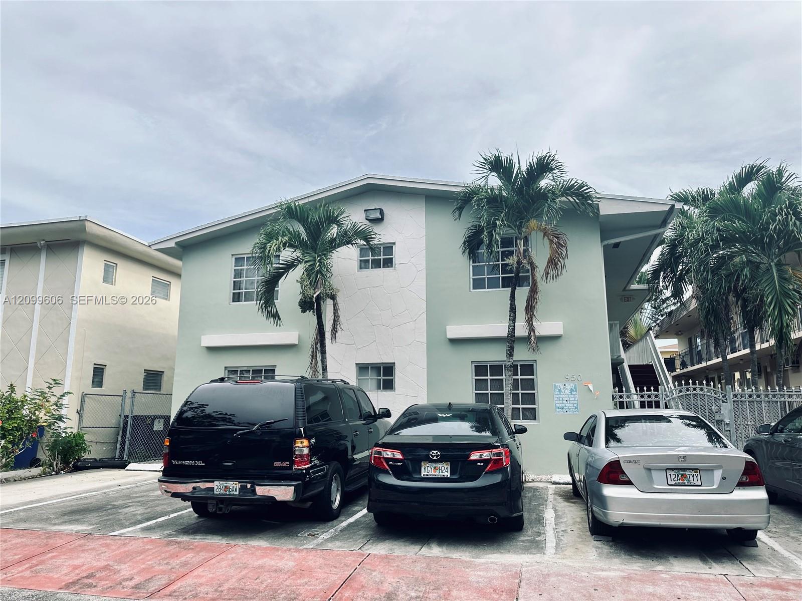 Pale mint-green two-story apartment building with palm trees and cars parked in front.