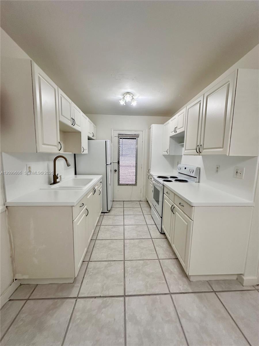 Galley kitchen with white cabinets, gray tile flooring, and an electric range.