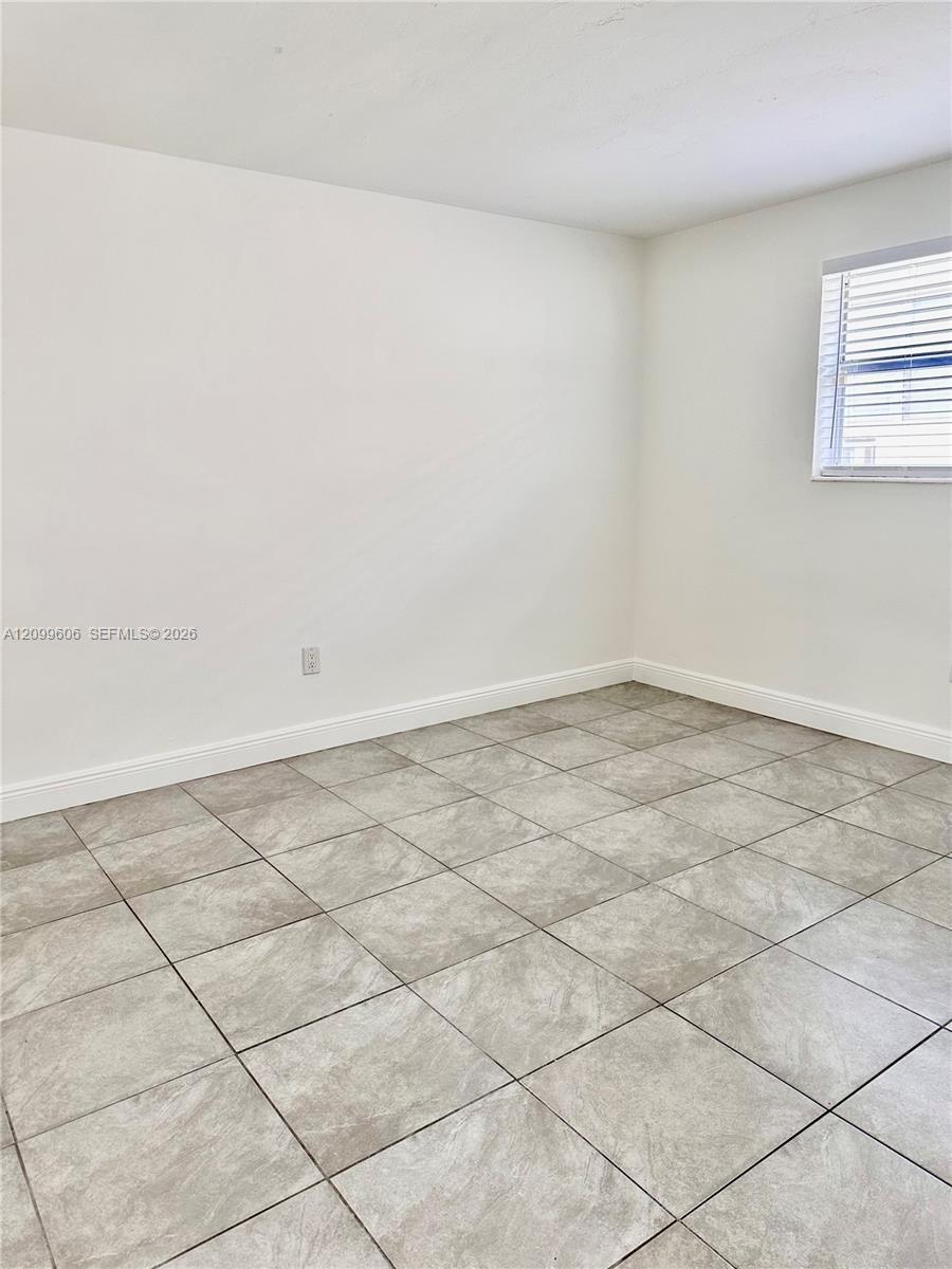 Empty room with gray-beige tile flooring and a small window with white blinds.