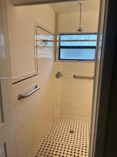Walk-in shower with white tile, metal grab bars, and a black-and-white patterned floor.
