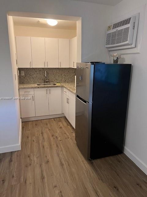 Compact kitchen with white cabinets, speckled stone counters, a refrigerator, and wood-look flooring.