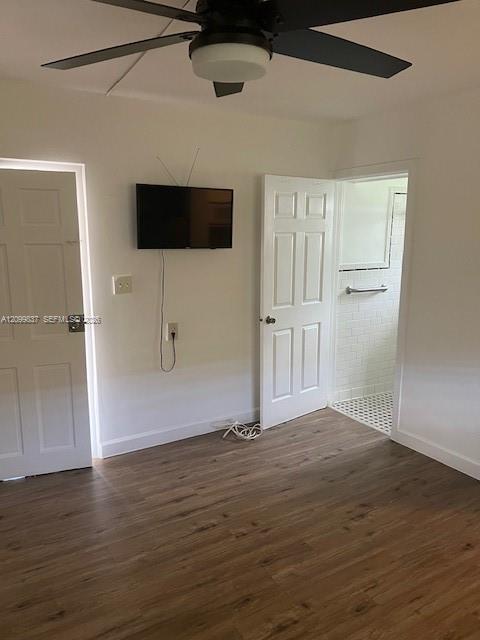 Unfurnished bedroom with wood-look flooring, ceiling fan, wall-mounted TV, and an open bathroom doorway.
