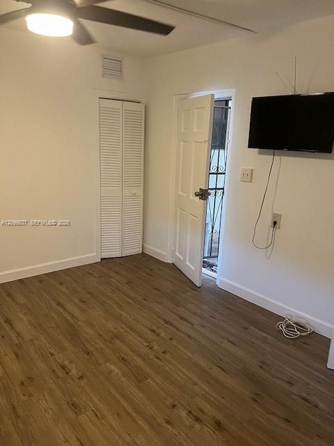 Nearly empty room with wood-look flooring, louvered closet doors, and an open exterior door.