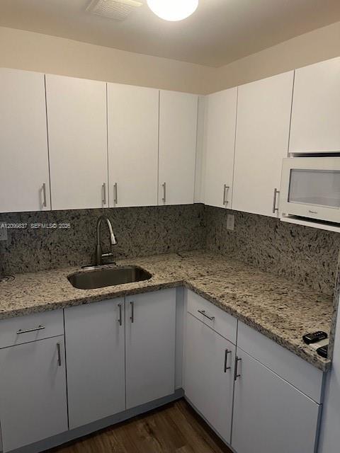 Compact kitchen with white cabinets, speckled countertops, a stainless steel sink, and wood-look flooring.