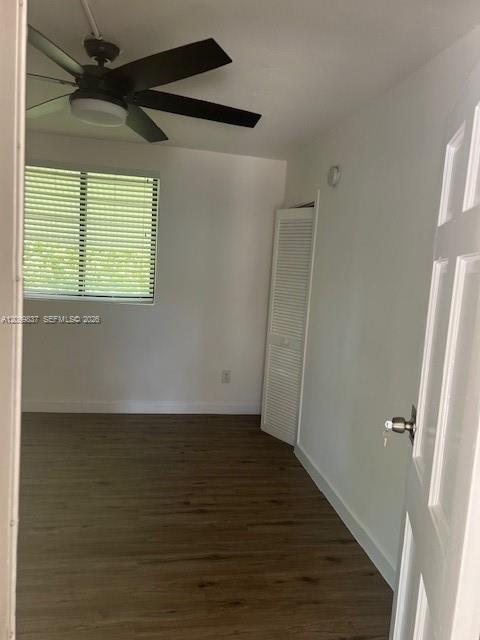 Empty bedroom with dark flooring, a black ceiling fan, window blinds, and a louvered closet door.